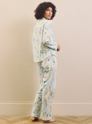 Woman wearing a light blue floral pyjama set against a beige wall.