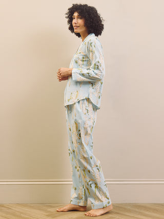 Woman wearing a light blue floral pyjama set against a beige wall.