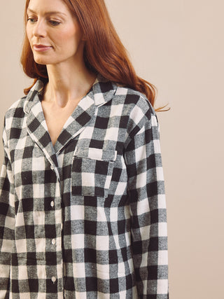 A woman wearing a black and white gingham check long-sleeve button-up nightshirt, shown from the chest up against a solid beige background.