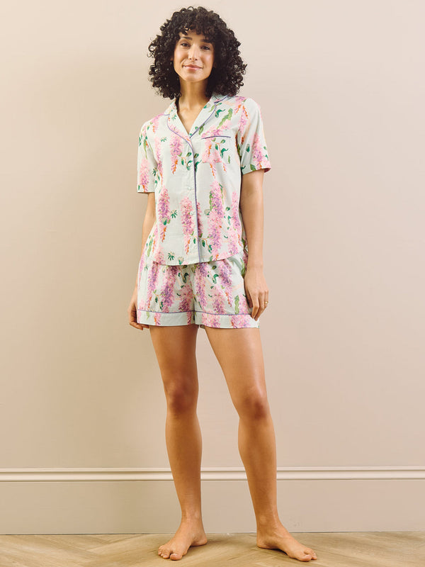 model wears floral wisteria print short pyjamas against a beige wall.