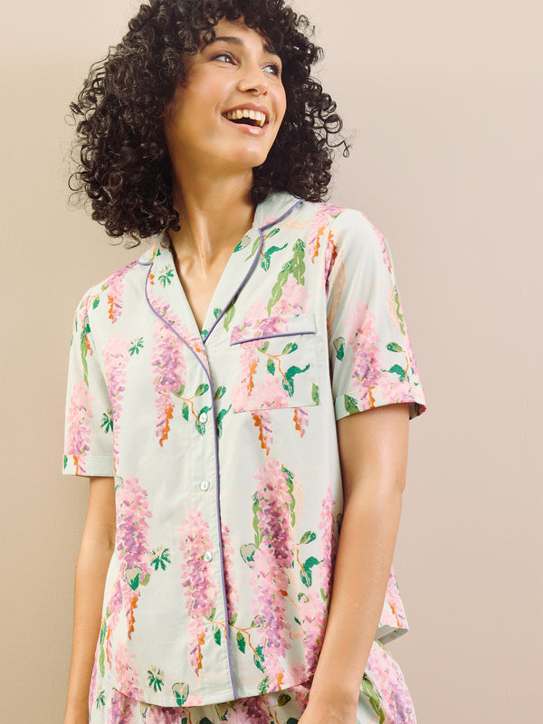 model wears floral wisteria print short pyjamas against a beige wall.