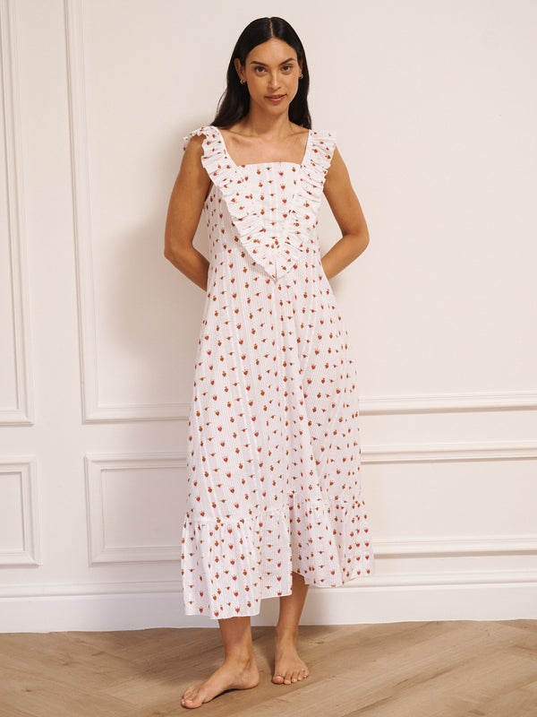 Model wearing white cotton seersucker nightdress with tiny sacred heart print, V-shaped frill neckline and midi-length hem, photographed against a neutral studio wall.