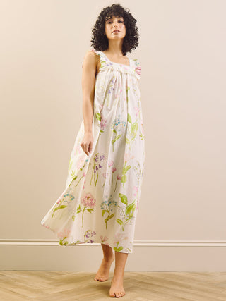 Woman wearing a floral night dress standing against a plain wall.