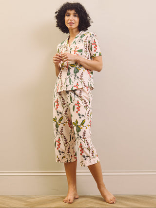 Woman wearing a pear & floral capri pyjama set against a plain wall.