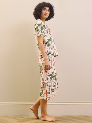 Woman wearing a pear & floral capri pyjama set against a plain wall.