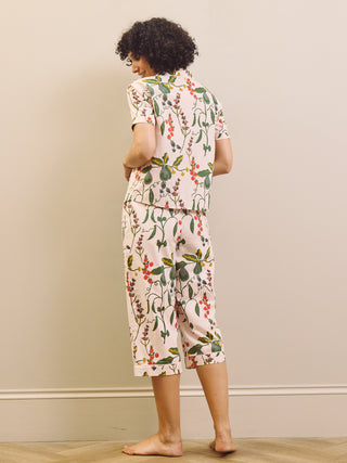Woman wearing a pear & floral capri pyjama set against a plain wall.