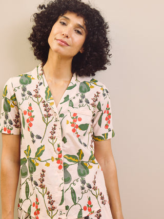 Woman wearing a pear & floral capri pyjama set against a plain wall.