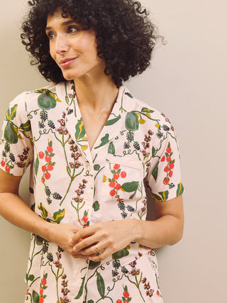 Woman wearing a pear & floral capri pyjama set against a plain wall.
