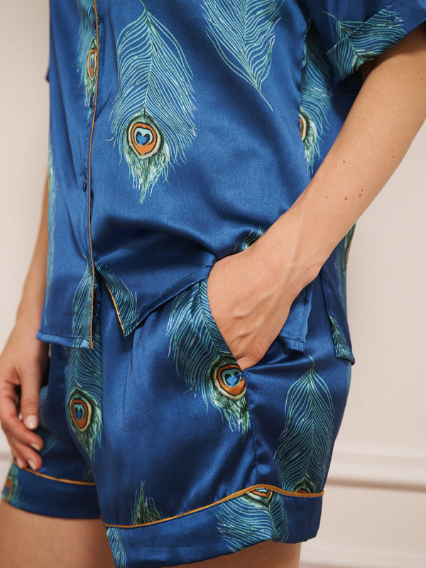 Model wearing a blue satin short pyjama set with peacock feather pattern against a white background. pocket detail
