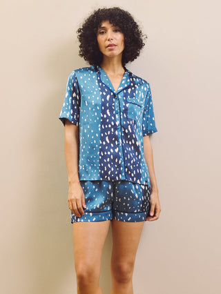 Woman wearing a blue patterned pajama set against a beige wall.