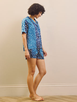 Woman wearing a blue patterned short pyjama set against a beige wall.