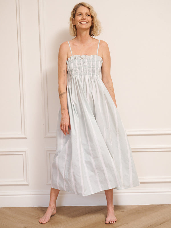 Model wearing a light blue striped dress standing against a white wall.