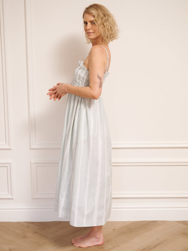 Model wearing a light blue striped dress standing against a white wall. Side detail