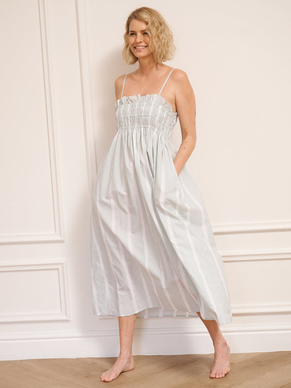 Model wearing a light blue striped dress standing against a white wall.