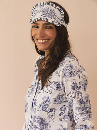 Woman wearing a blue floral toile eye mask and matching pyjamas against a beige background