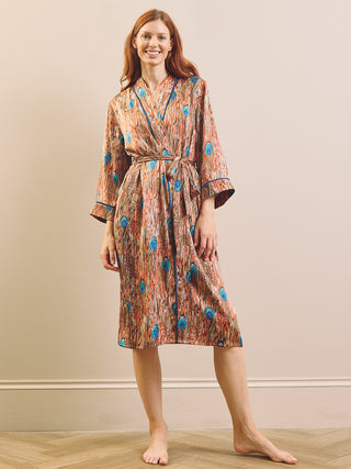 A woman modelling a knee-length patterned dressing gown robe with a tie waist and three-quarter sleeves, standing barefoot against a plain beige wall and light wood floor.
