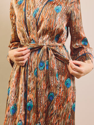 A close-up of a person wearing a long-sleeve wrap dressing gown with a peacock feather print in brown, orange, and blue, tied at the waist.