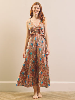 A woman modelling a sleeveless maxi nightdress with a brown and orange abstract pattern and blue circular accents, standing barefoot against a beige wall.