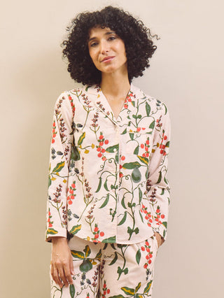 Woman wearing a pear & floral pyjama set against a plain wall.