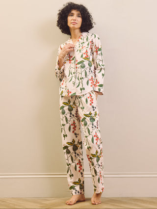 Woman wearing a pear & floral pyjama set against a plain wall.