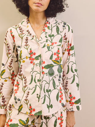 Woman wearing a pear & floral pyjama shirt against a plain wall.