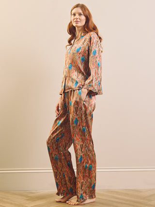 A woman modelling a two-piece pyjama set with a rust-orange abstract pattern and blue circular accents, standing barefoot against a plain beige wall.