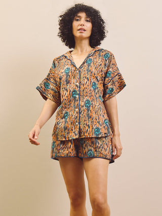 Woman wearing a feather patterned short pyjama set standing against a plain wall.