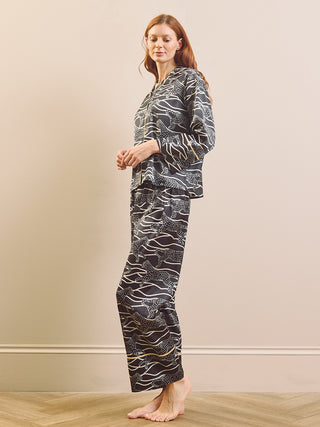 A person wearing a matching pyjama set with a black base and white abstract animal print, shown from the chest down against a plain beige studio background.