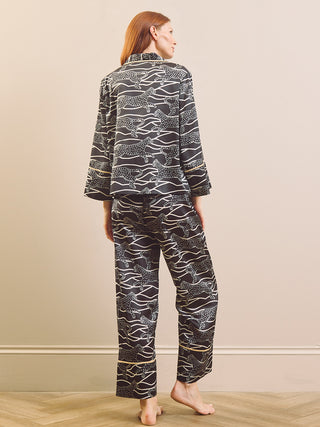 A person wearing a matching pyjama set with a black base and white abstract animal print, shown from the chest down against a plain beige studio background.