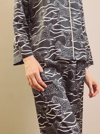 A person wearing a matching pyjama set with a black base and white abstract animal print, shown from the chest down against a plain beige studio background.