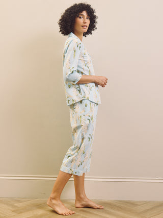 Woman wearing a light blue floral wisteria capri pyjama set against a beige wall.