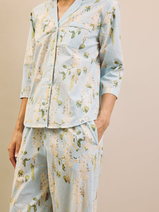 Woman wearing a light blue floral wisteria capri pyjama set against a beige wall.
