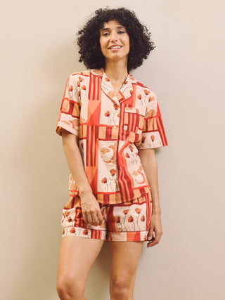 Woman wearing a rust and cream patch work patterned pyjama set against a plain wall.