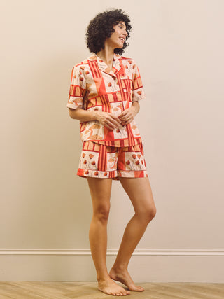 Woman wearing a rust and cream patch work patterned pyjama set against a plain wall.