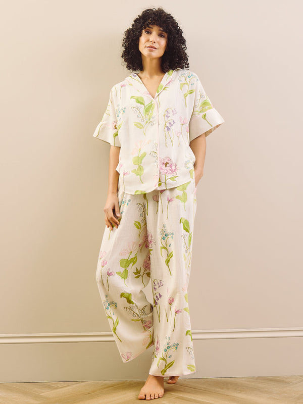 model wears relaxed fit pyjama set in a pretty floral print against a beige wall. 