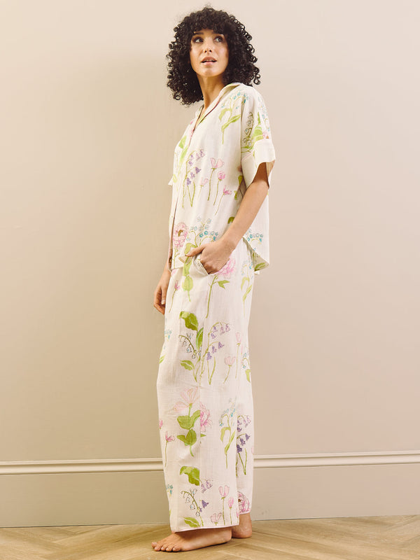 model wears relaxed fit pyjama set in a pretty floral print against a beige wall. 