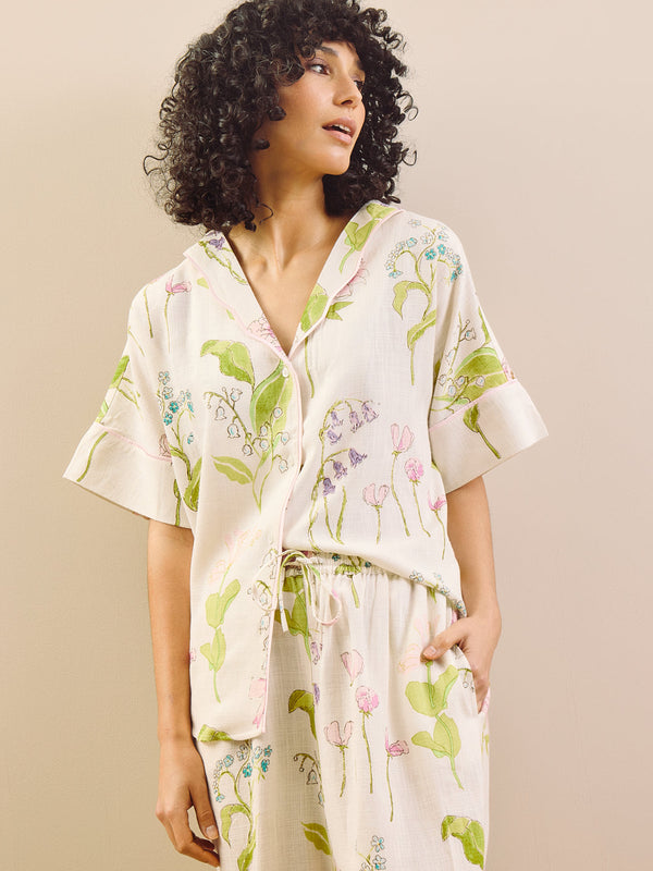 model wears relaxed fit pyjama set in a pretty floral print against a beige wall. 