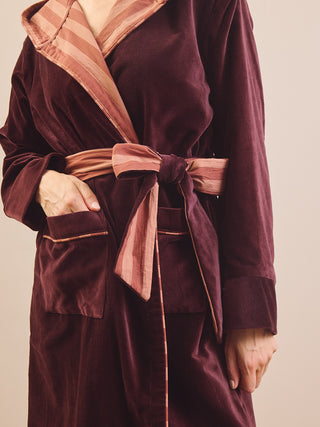 A close-up of a person wearing a plush velvet robe in deep burgundy with contrasting dusty rose striped trim and a matching tie belt.