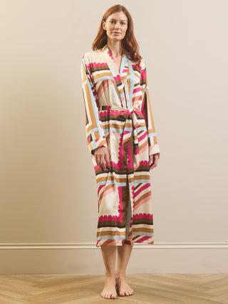 A woman stands barefoot in a studio wearing a long-sleeve wrap robe with a multicolor geometric pattern on a beige base.