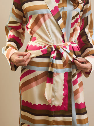 A close-up of a model wearing a long-sleeved wrap robe with a bold retro striped pattern in beige, brown, pink, and light blue, tied at the waist.
