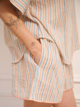 Women’s pastel stripe cotton gauze shortie pyjama set with oversized button-up top, short sleeves, open collar and matching shorts with pockets, shown on model indoors. pocket detail. 
