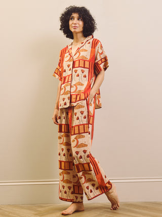 Woman wearing a rust and cream patch work patterned pyjama set against a plain wall.