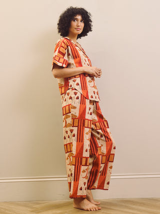 Woman wearing a rust and cream patch work patterned pyjama set against a plain wall.