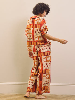 Woman wearing a rust and cream patch work patterned pyjama set against a plain wall.