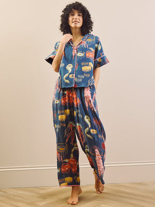 Woman wearing a blue pajama set with a colourful ocean creature pattern on a plain background