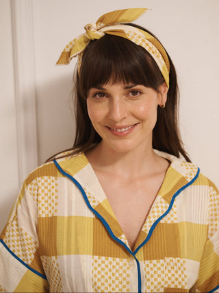 Woman wearing a yellow patterned outfit with a matching headband against a plain background