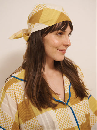 Woman wearing a yellow and white patterned bandana and matching outfit against a plain background
