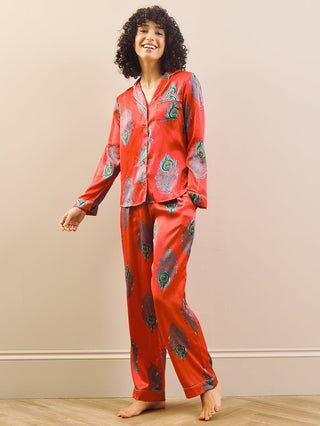 model wears long leg satin pyjamas in red with a peacock print.