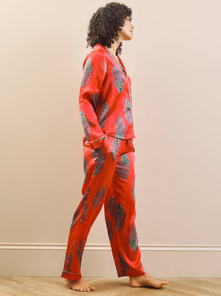 model wears long leg satin pyjamas in red with a peacock print.