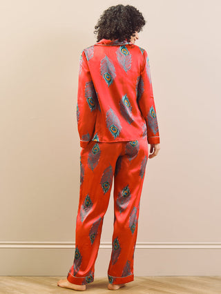 model wears long leg satin pyjamas in red with a peacock print.
